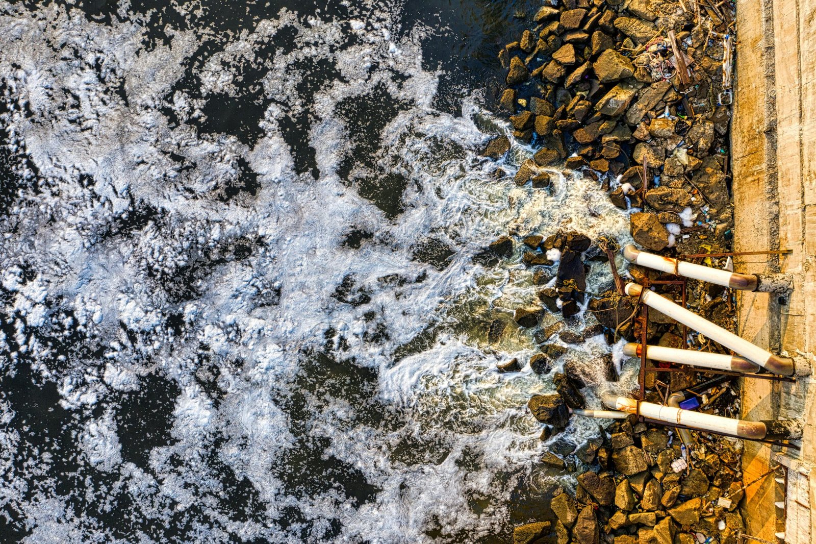 Aerial view of polluted water flowing through pipes into a Jakarta river, causing environmental concerns.